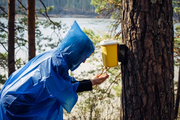 vrouw in blauwe regenjas wast haar handen in de wasbak die aan de boom hangt.