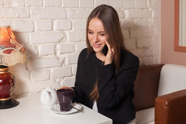 Vrouw in café die thee drinkt en haar smartphone gebruikt