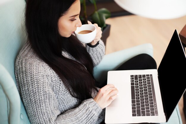 Vrouw in casual kleding die laptop gebruikt en glimlacht terwijl ze binnenshuis werkt.