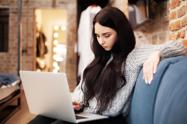 Vrouw in casual kleding die laptop gebruikt en glimlacht terwijl ze binnenshuis werkt.