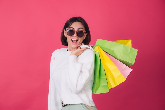 Vrouw in casual witte trui en zonnebril op rode muur