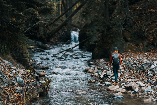 Vrouw in de bergen bij de rivier met een rugzak op haar rug en een bos op de achtergrond