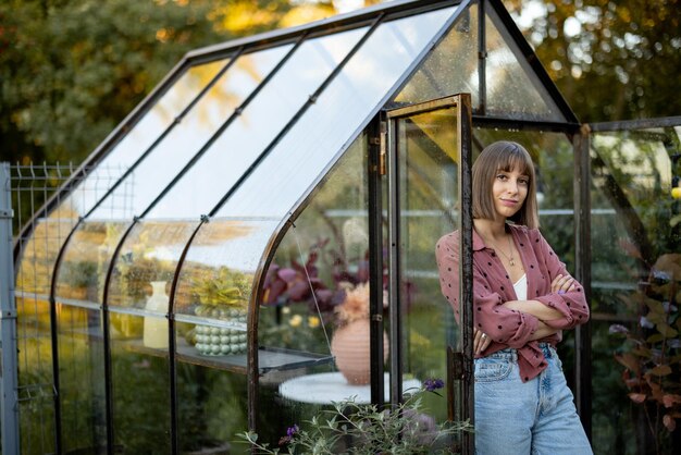 Vrouw in de buurt van kas met bloemen in achtertuin