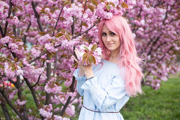 Vrouw in de buurt van roze sakura bloeiende boom in blauwe jurk