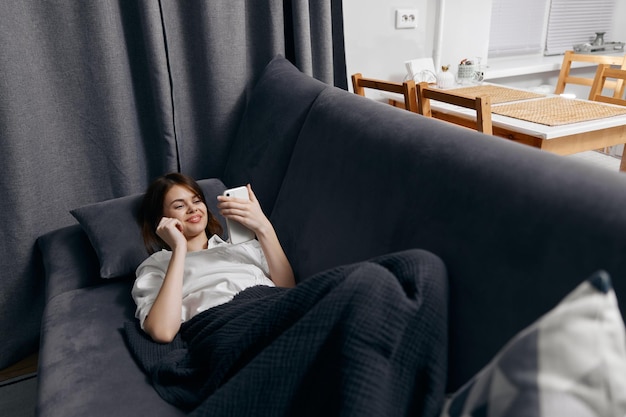 Vrouw in de kamer ligt op de bank met een telefoon in haar hand