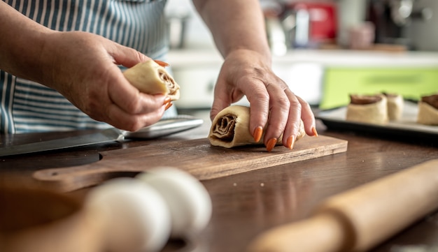 Vrouw in de keuken snijdt voorzichtig rauw deeg om heerlijke zelfgemaakte kaneelbroodjes te maken