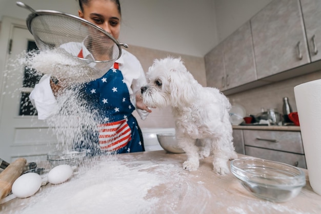 Vrouw in de keuken zeeft bloem samen met een hond