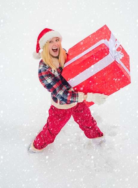 Vrouw in de sneeuw Portret van een kerstmanvrouw met een enorm rood cadeau die naar de camera kijkt Kerstvrouw met a