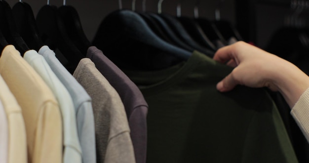 Foto vrouw in de winkel kijkt door de mannelijke kleren die op de rekken hangen thuis kast of garderobe