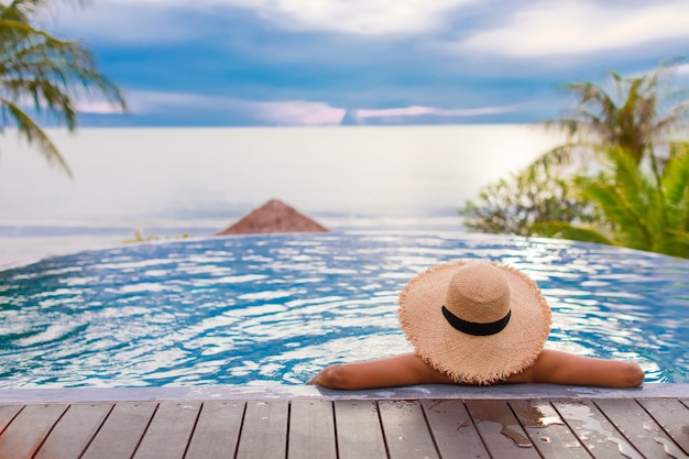 Vrouw in de zwembaden met de zomerhoed kijken naar de zee met blauwe lucht.