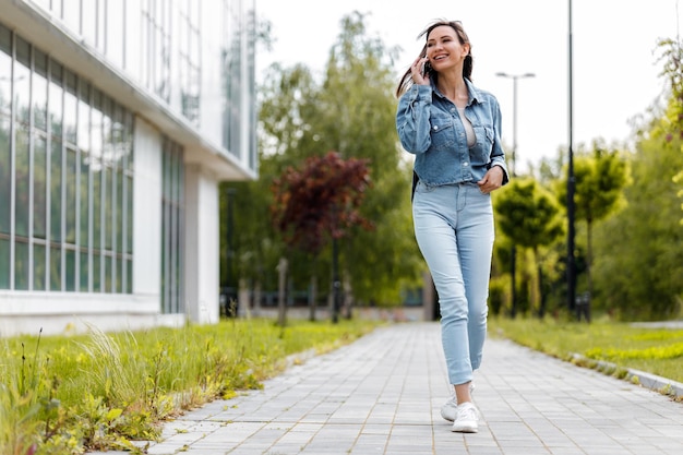 Vrouw in denim loopt en praat aan de telefoon in een stedelijke omgeving