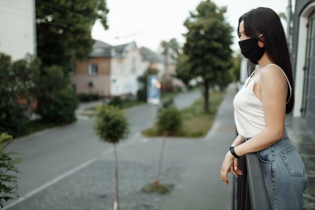 vrouw in een beschermend masker op een balkon kijkt naar een lege stad