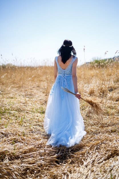 Vrouw in een blauwe lange jurk in het riet. Modeportret met gedroogde bloemen