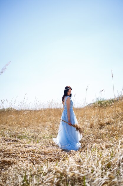 Vrouw in een blauwe lange jurk in het riet. Modeportret met gedroogde bloemen