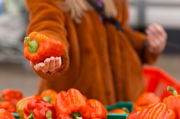 Vrouw in een bontjas houdt rode paprika in een winkel