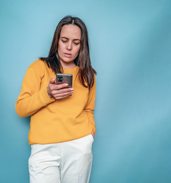 Vrouw in een gele trui houdt een telefoon in haar hand en typt een bericht