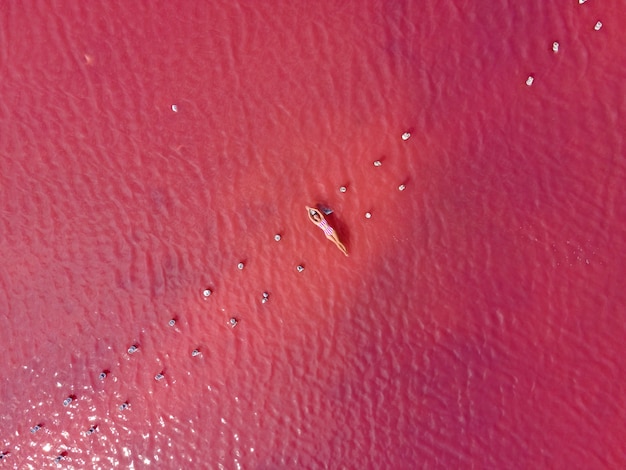 Vrouw in een gestreept badpak ligt op een roze meer dat van bovenaf is genomen vanuit een drone