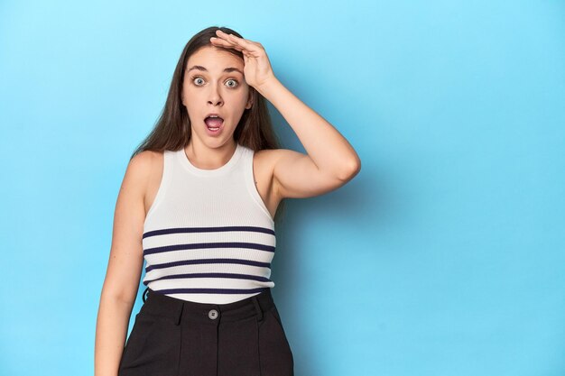 Vrouw in een gestreepte top poseert op een blauwe studio achtergrond schreeuwt luid houdt ogen open