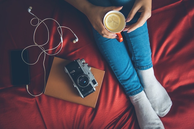 Vrouw in een gezellige trui op het bed met het oude boek en een kopje thee met melk in hun handen, bovenaanzicht