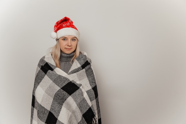 Vrouw in een grijze wollen trui en een kerstmuts bevroor en wikkelde zichzelf in een plaid