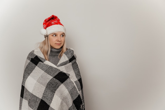 Vrouw in een grijze wollen trui en een kerstmuts bevroor en wikkelde zichzelf in een plaid