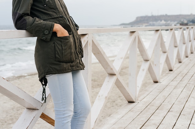 Vrouw in een groen jasje en jeans die zich op de houten promenade dichtbij het overzees bevinden