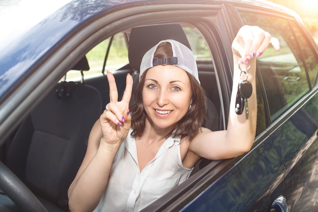 vrouw in een hoed met sleutels tot nieuw gekochte auto en glimlachend in de camera