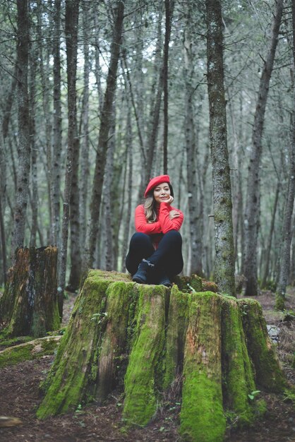 Vrouw in een kalme en bedachtzame houding op een bemoste stronk midden in het bos