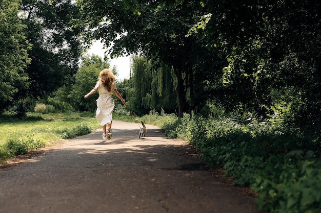 Vrouw in een lange witte jurk loopt terug met een kattenras Scottish Straight in het park in de zomer