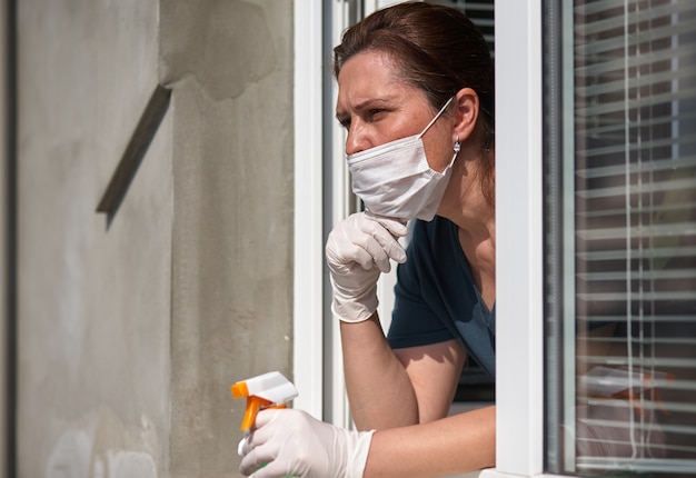 Vrouw in een medisch gezichtsmasker kijkt uit het raam.