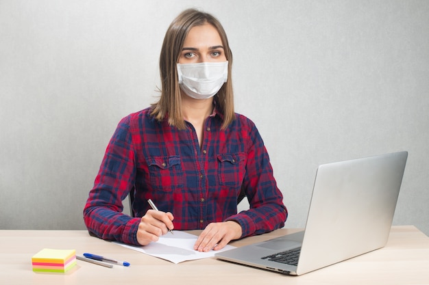 Vrouw in een medisch masker werkt vanuit huis met computer