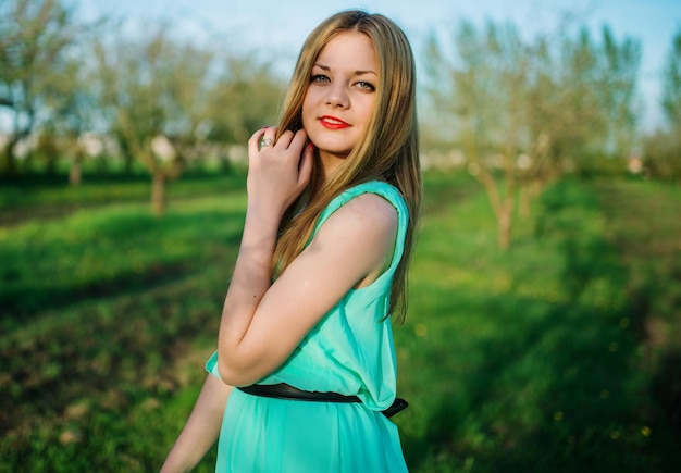 Vrouw in een mooie lange turkooizen jurk die zich voordeed op een weide in de fruittuin