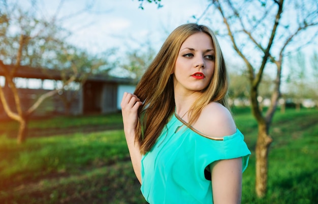 Vrouw in een mooie lange turkooizen jurk die zich voordeed op een weide in de fruittuin