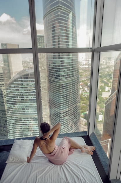 Vrouw in een nachtjapon liggend op het bedraam in een wolkenkrabber bij het bed