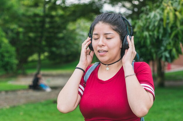 vrouw in een park luistert naar muziek, zingt met haar ogen dicht, houdt een koptelefoon vast.