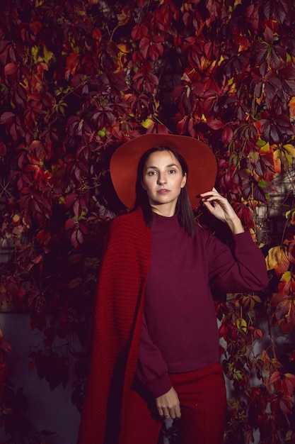 Vrouw in een rode hoed en rode trui staat op een achtergrond van oranje bladeren druiven muur herfst