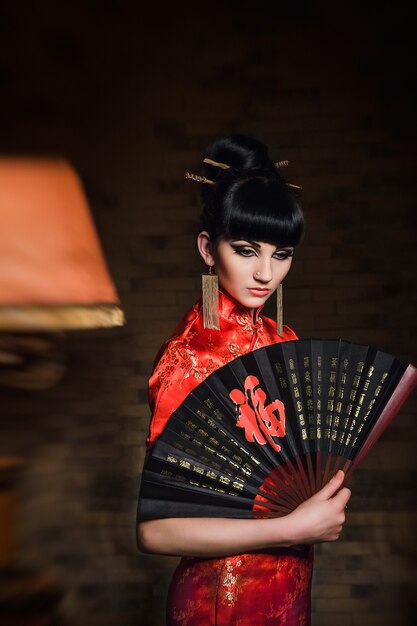 vrouw in een rode Japanse zijden jurk qipao in een donkere sfeervolle kamer