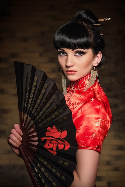 vrouw in een rode Japanse zijden jurk qipao in een donkere sfeervolle kamer