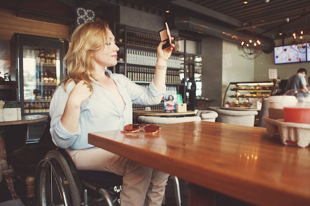 Vrouw in een rolstoel is koffie drinken en selfie maken op een smartphone in een café.