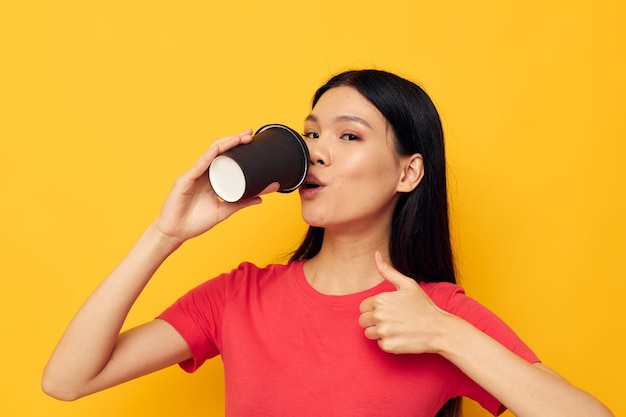 Vrouw in een rood t-shirtglas met een drank gele achtergrond