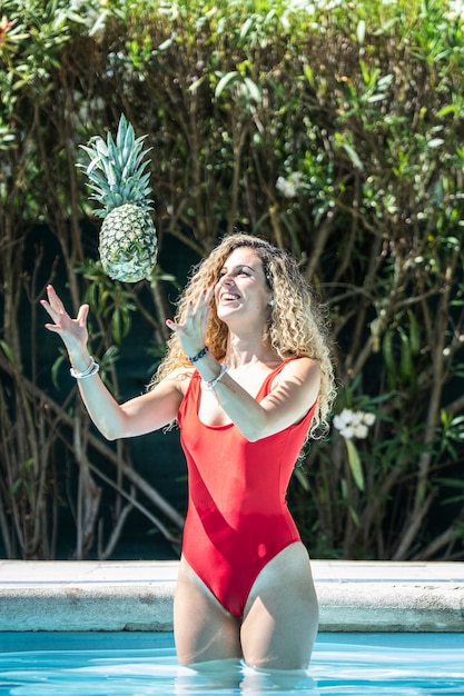 Vrouw in een rood zwempak die een ananas in de lucht werpen in een pool