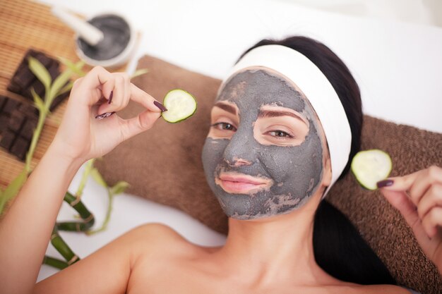 Vrouw in een schoonheidssalon, wellness. Cosmetische procedure vrouwengezicht in het masker verzachtend en plakjes komkommer op de ogen