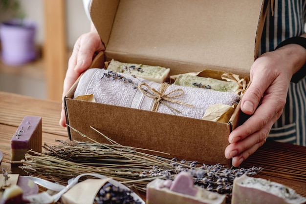 Vrouw in een schort houdt een knutseldoos vast met een handdoek en stukjes natuurlijke lavendelzeep Handgemaakt geschenkverpakkingsconcept