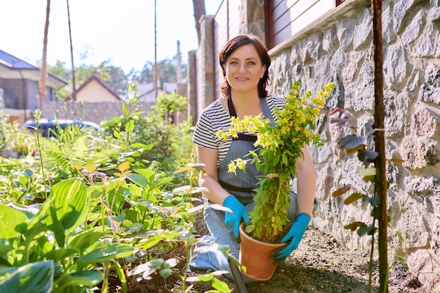 Vrouw in een schort van tuinhandschoenen met een schop die bloeiende planten plant