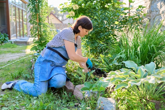 Vrouw in een schort van tuinhandschoenen met een schop die bloeiende planten plant