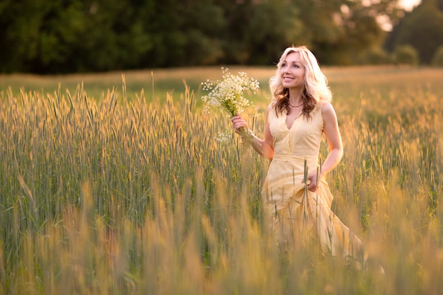 Vrouw in een strooien hoed in een bloemenveld met een boeket wilde bloemen