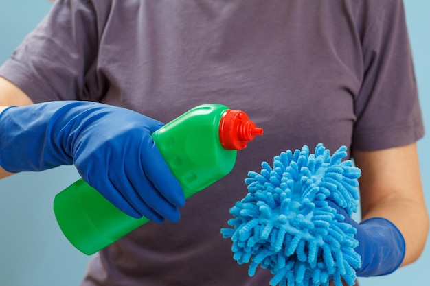 Vrouw in een t-shirt met een plastic fles wasvloeistof en een doek op de blauwe achtergrond