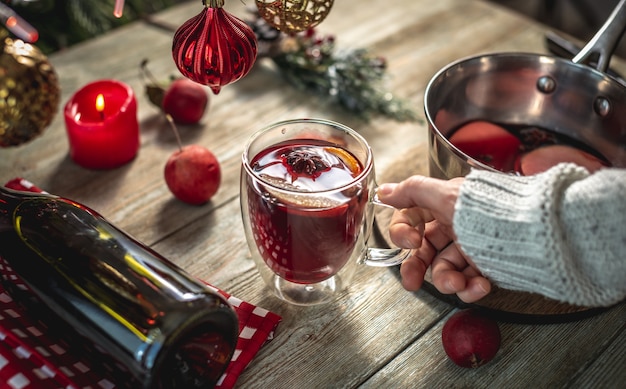 Vrouw in een trui houdt een doorzichtige mok vast met geurige pittige glühwein versierd met fruit en kruiden. Concept van een gezellige feestelijke sfeer, nieuwjaars- en kerstsfeer.