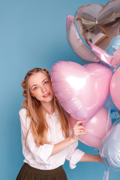 Vrouw in een wit overhemd met een bos ballonnen op een blauwe ondergrond