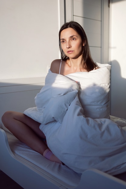 Vrouw in een wit t-shirt ligt op bed en een kussen ligt onder de deken in de kamer